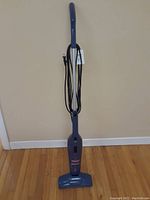 Full view of the upright vacuum showing the entire vacuum from base to handle including the power cord wrapped around the back side.