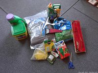 Various garden supplies including two Miracle-Gro fertilizer containers, bag of potting soil, pruning shears, gloves, seed pellets, seed packets, scissors, and planting labels.