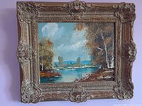 Frontal view of the framed oil painting showing a landscape with trees, lake, mountains, and cloudy sky