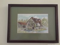 Framed watercolour painting showing a stone house with a red roof and greenery, nicely preserved in a wooden frame with an olive green mat.