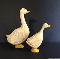 Front view of two carved wooden geese on black background.
