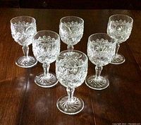 Six clear antique pressed glass goblets arranged on a wooden surface showing the full set.