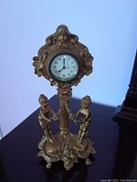 Full view of the vintage ornate clock on dark surface against a wall showing the two child figurines and floral motifs.