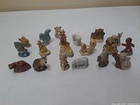 Collection of 15 small ceramic figurines arranged on a white surface, showing variety of animals and characters with detailed paint and glossy finish.