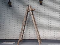 Photo showing full view of the wooden step ladder standing open with all steps visible, against a brick wall.
