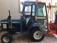 Side view of blue Ford 1210 tractor with enclosed cab and white wheels