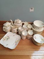 Full set of porcelain dishes including coffee pot, teapot, creamer, multiple cups, small bowls, side plates, serving plate, and serving bowl all with floral and butterfly patterns and gold trim on white background.