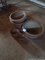 Six clay flower pots grouped together on the floor, showing size differences and condition.
