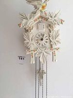 White wooden cuckoo clock showing carved leaf design, clock face with Roman numerals, and bird door at top.