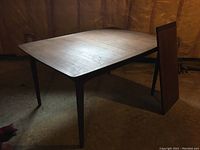 Full view of table with leaf leaning beside it in basement setting
