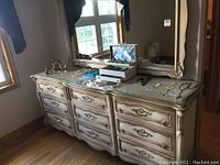 Wide view of the dresser topped with mirror, showing nine drawers and multiple decorative objects on top