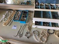 Photo showing assorted pearl and bead necklaces, jewelry box with multiple compartments and some bracelets