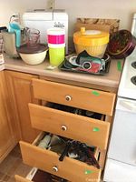 Overview of kitchen counter and open drawers showing various kitchenware including bread maker, mixer, salad spinner and storage containers