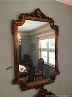 Full view of the large bronze painted ornate framed mirror hanging on the wall reflecting a dining room setting.