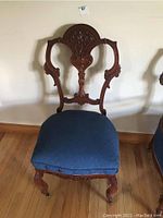 Front view of parlour chair displaying intricate carved wooden backrest and blue upholstered seat.