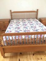 Full view of queen size oak bed frame with mattress showing floral bedding and matching nightstands