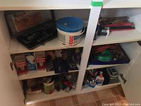 Photo of white cabinet shelves containing tools, lightbulbs, drywall compound, glue and other items.