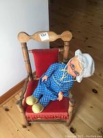 Child's wooden chair with red velveteen seat and backrest, showing wear and fabric fringe, with Mrs. Beasley doll seated.