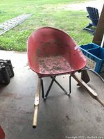 Front view of red metal basin of the wheelbarrow showing dirt and wear inside with wooden handles extending outward.