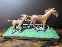 Front angle view of folk art wooden carving showing galloping horse and colt on green base