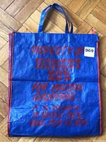 Full view of the large blue woven plastic bag with red text, showing handles and structure.