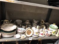 Wide view of large assortment of porcelain and china plates, cups, bowls, teapots, and decorative items on shelf
