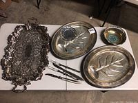 Overview of all silver plated items including trays, utensils and bowl on table