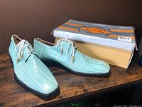 Pair of mint green men's shoes with crocodile pattern sitting beside original Yashi shoe box
