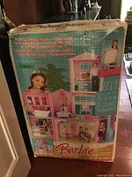 Front and side views of the original box of the Barbie 3-Story Dream House showing the product images and branding in multiple languages.