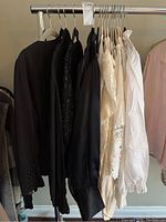 Hanging rack with five blouses, including black and cream colors, various textures and sleeve lengths