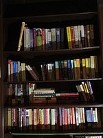 Four shelves of assorted books with varied titles and colors, showing mixed genres including cooking, novels, and non-fiction.