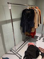 Metal clothing rack against a wall with clothes hanging on the bar.