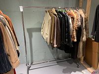 Full view of the metal clothing rack holding assorted coats and jackets showing its size and structure.