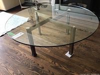 Photo showing the round glass top coffee table with metal frame and wooden floor background.