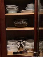 Shelves with various Corningware dishes including round and square casserole dishes with Cornflower and Spice of Life patterns, and a clear Pyrex glass bowl with white floral decoration.
