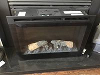 Front view of the black framed electric fireplace insert, showing artificial logs inside behind glass.