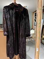 Full view of a long dark brown mink fur coat hanging on a wooden hanger in a basement environment.
