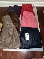 Overview of six pairs of ladies leather pants folded, showcasing all colors including brown, dark blue, taupe, red, pink, and dark purple.