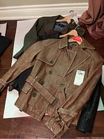 Four women's leather jackets lying flat, showing the brown belted jacket on top and other jackets in dark colors beneath.
