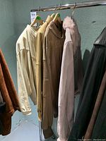 Four leather jackets hanging on rack in basement, showing a range of colors from cream to tan to pink and black.
