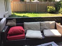 Front view of three-section dark brown wicker style outdoor couch with beige and red cushions arranged on the deck.