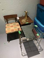 Shows the wood framed chair with plaid padded seat, telephone table, metal side table missing top, and metal decor items including a brass pitcher, fan, and mirror