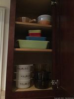 Cabinet shelves showing various bowls including white floral patterned bowls, amber glass casserole dish, nested colored bowls, and bakeware.