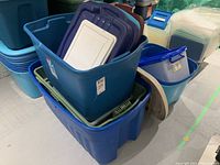 Seven large plastic storage containers stacked and nested with assorted lids on top, mostly blue containers with colored lids.