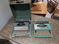 Photo showing two vintage typewriters on a table: Underwood in a metal case and Smith-Corona without cover.
