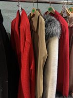 Four women's coats hanging on rack including coral coat size 46, beige trench coat, white jacket with grey fur, and red jacket