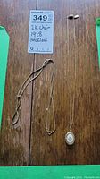 Two gold-tone necklaces laying flat on wooden surface, one plain 12k chain and one with floral locket and 1928 tag