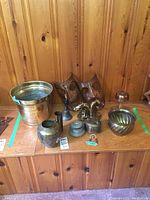 Photo showing various brass items including two horse bookends, planters, box, bell, horseshoe, and pipe stand arranged on wood surface.