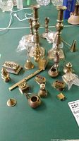 Photo showing a variety of brass miniatures including tall candle holders, small candle holders, a bell, envelope opener, snuffer, trinket box, and miniature brass teapot arranged on a table.