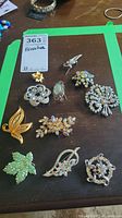 All eleven vintage brooches arranged on a black surface, showing variety in design and color including butterfly, floral, and leaf shapes.